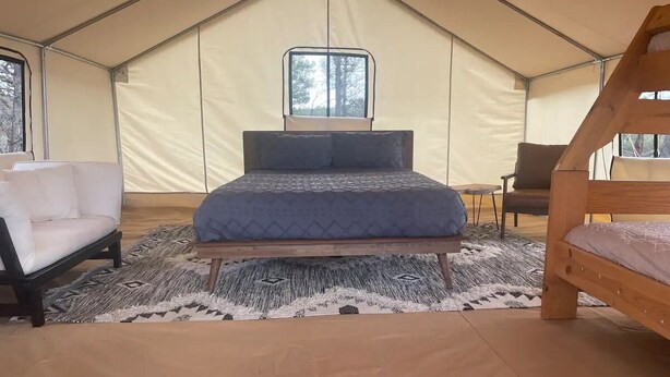 Une tente équipée d’un lit, d’une chaise et d’une petite table.