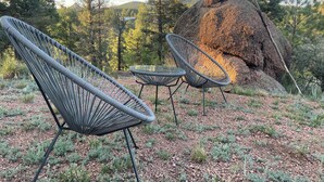 Un espace aménagé avec deux chaises et une petite table, le tout installé devant un grand rocher et des arbres.