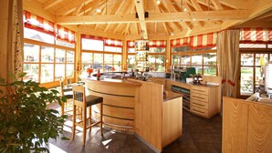 A wooden interior with a kitchen area, bar stools, and large windows. - Holiday apartment with wellness area (Ötz im Ötztal)