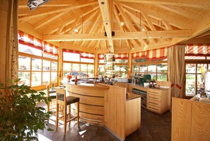 A wooden interior with a kitchen area, bar stools, and large windows. - Holiday apartment with wellness area (Ötz im Ötztal)