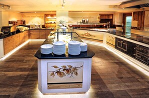 A buffet setup with plates stacked on a counter, surrounded by wooden cabinets and a decorative wall with a fruit branch design.