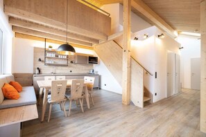 A modern kitchen with wooden cabinetry, a dining area with a table and chairs, and a staircase leading to another level. - Holiday apartment with sauna and fitness room (Hinterstoder)