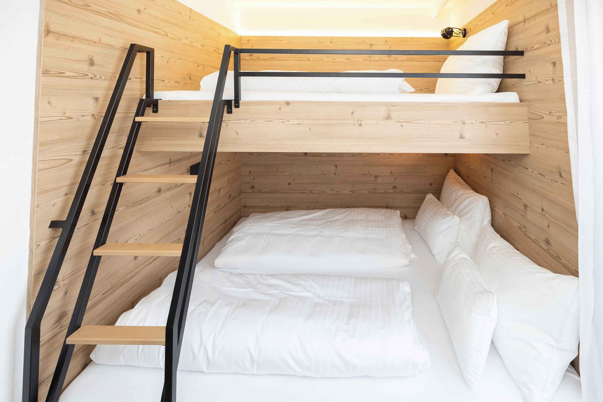 Een stapelbed met een houten trap en wit beddengoed.