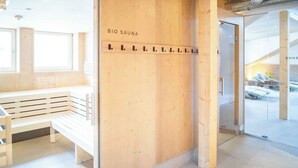 Um balcão de madeira com a indicação 'BIO SAUNA', um banco e uma porta de vidro que dá para uma área de sauna.