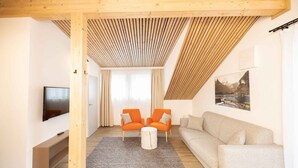 Uma sala de estar moderna com uma televisão, duas poltronas laranja, um sofá bege e teto de madeira.