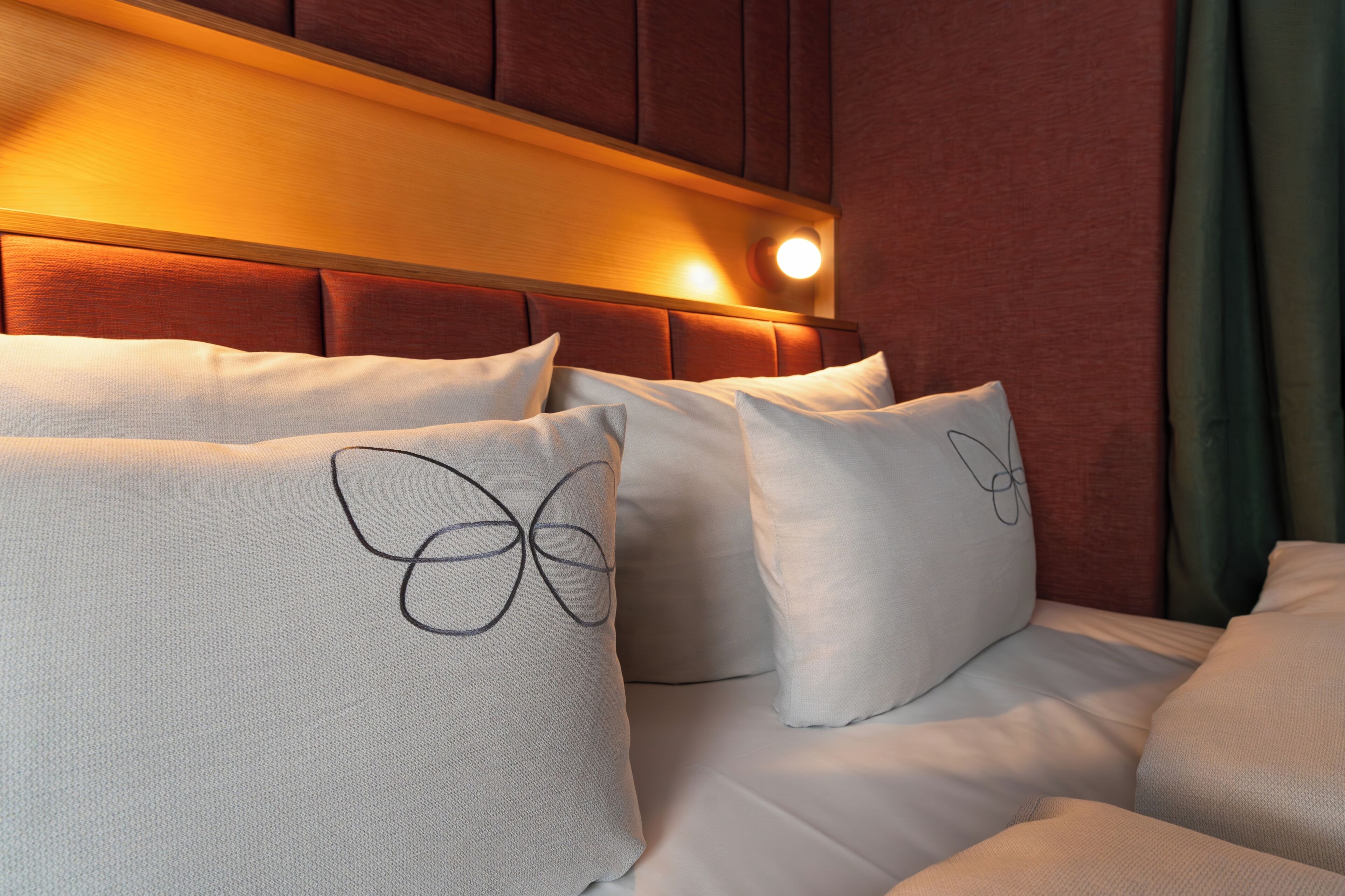 Habitación de hotel con una cama, almohadas con diseños de mariposas, un cabecero de madera y una cortina verde.
