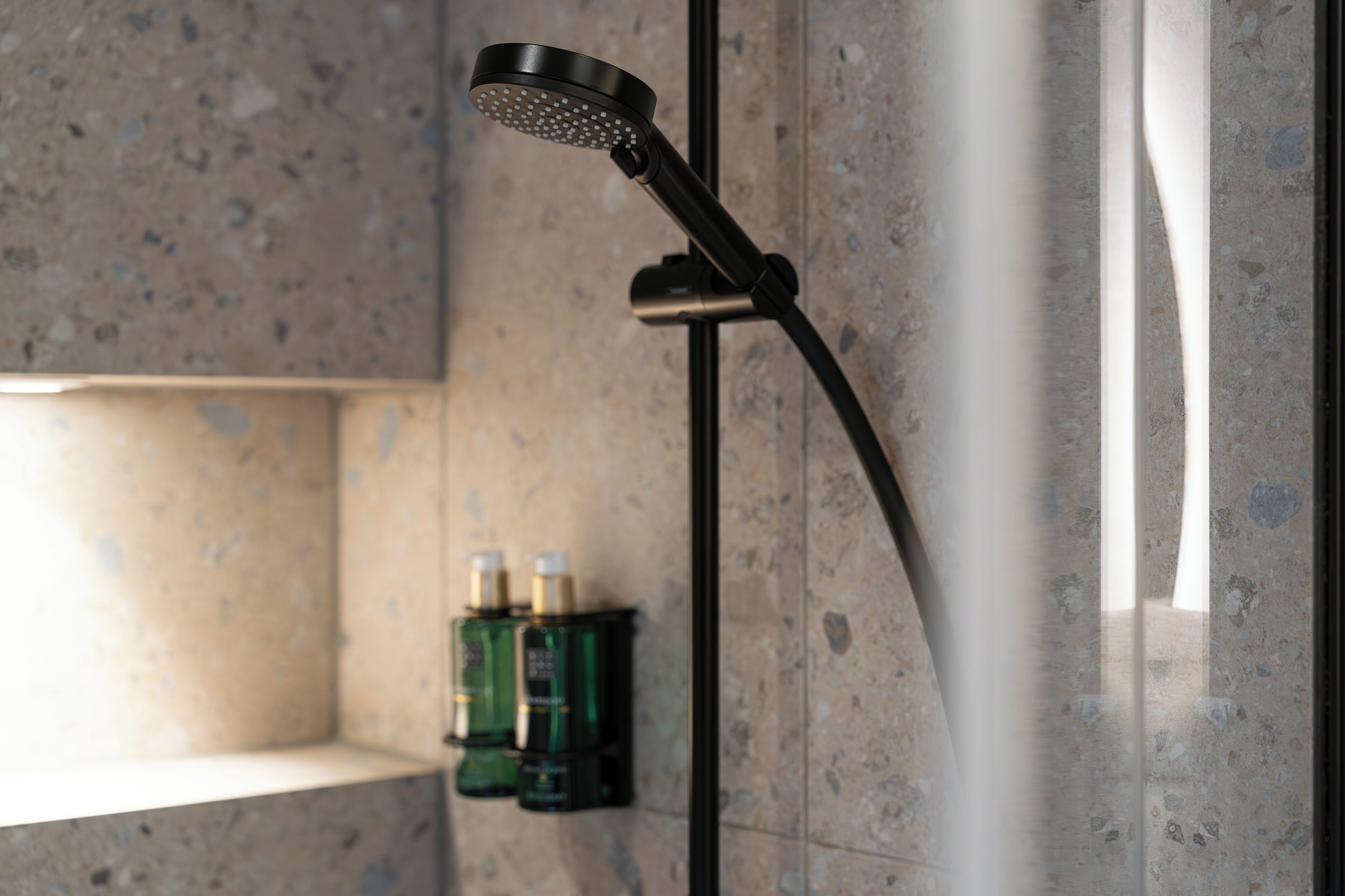 A modern showerhead with a curved design, mounted on a wall with a speckled tile pattern.