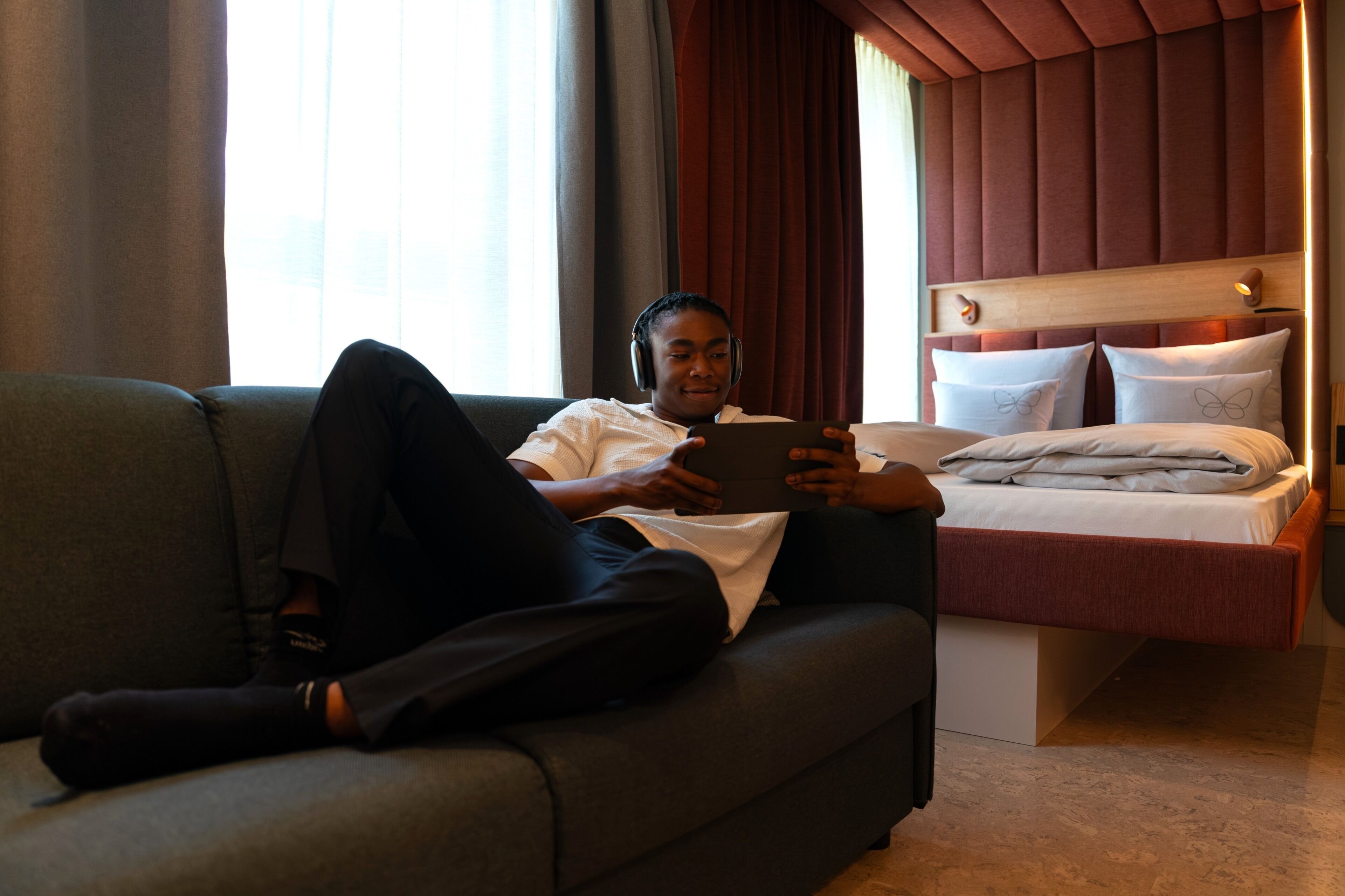 A person sitting on a sofa in a room with a bed and a headboard with lights.