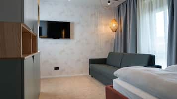 Una habitación de hotel moderna con una televisión de pantalla plana montada en la pared, un sofá, una cama y una mesita de noche.