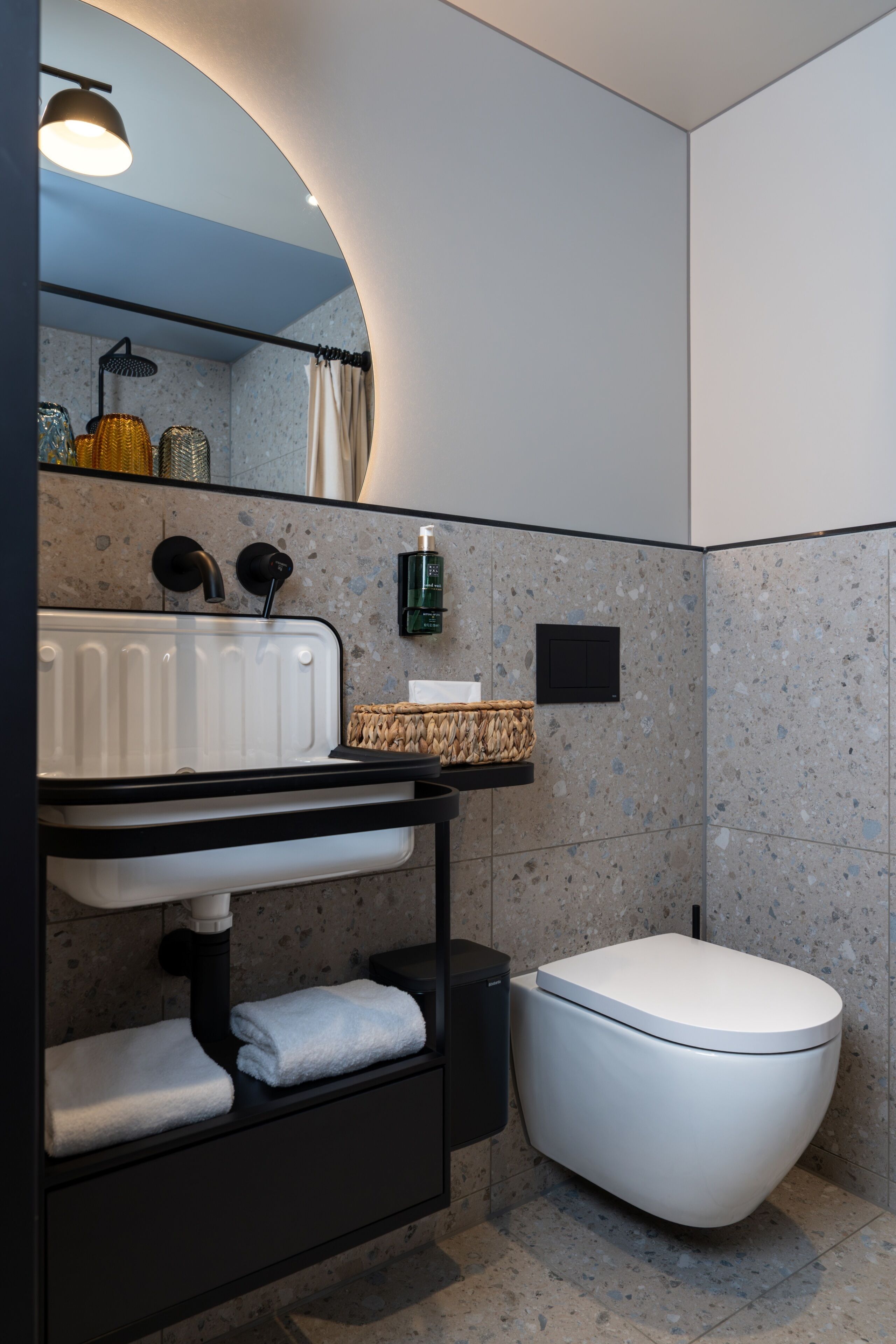 Un baño moderno con un lavamanos blanco, encimera negra y un inodoro blanco.
