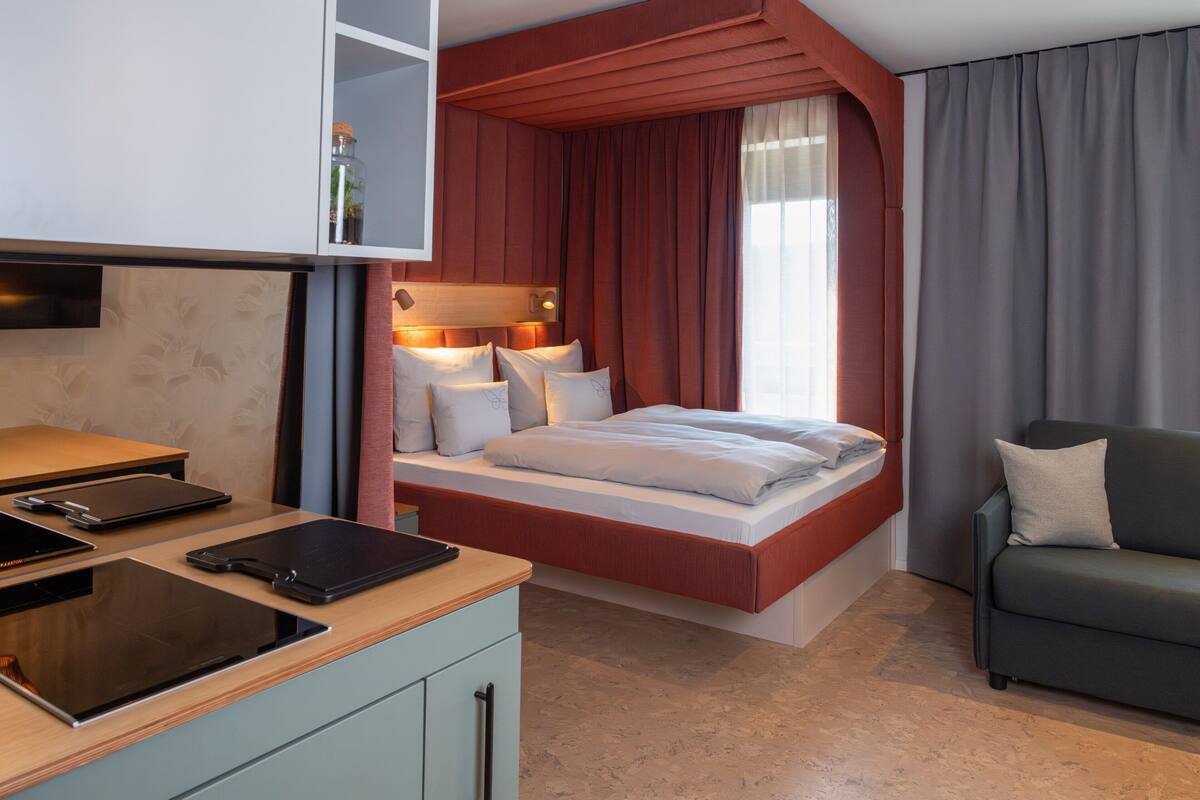 A modern hotel room with a bed, a desk, a chair, and a window with curtains.
