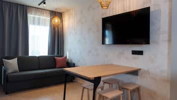 A modern living room with a sofa, a TV mounted on the wall, a wooden table with stools, and a patterned wallpaper.