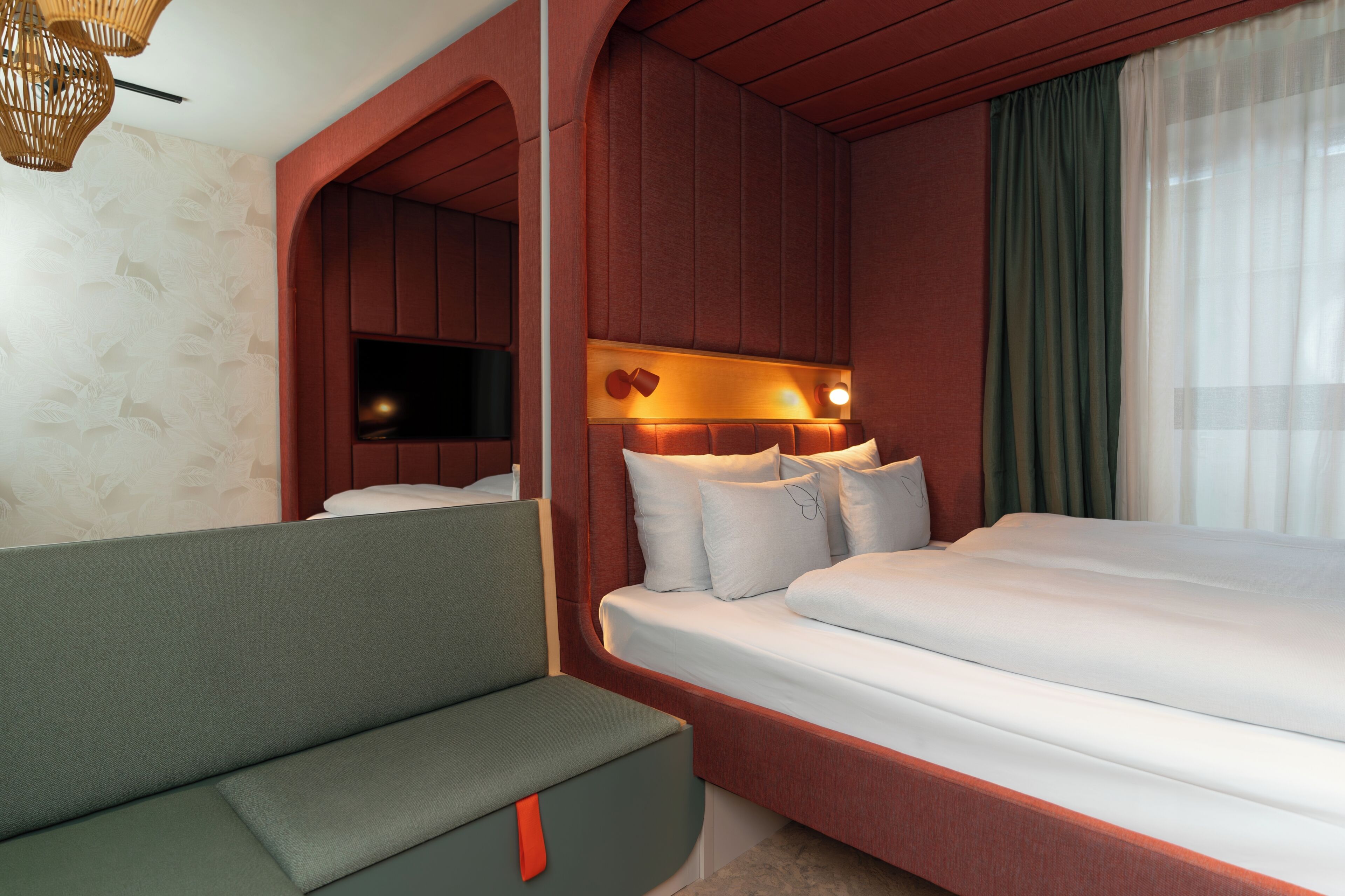 A modern hotel room with a bed, a seating area, a television, and a wall-mounted light fixture.