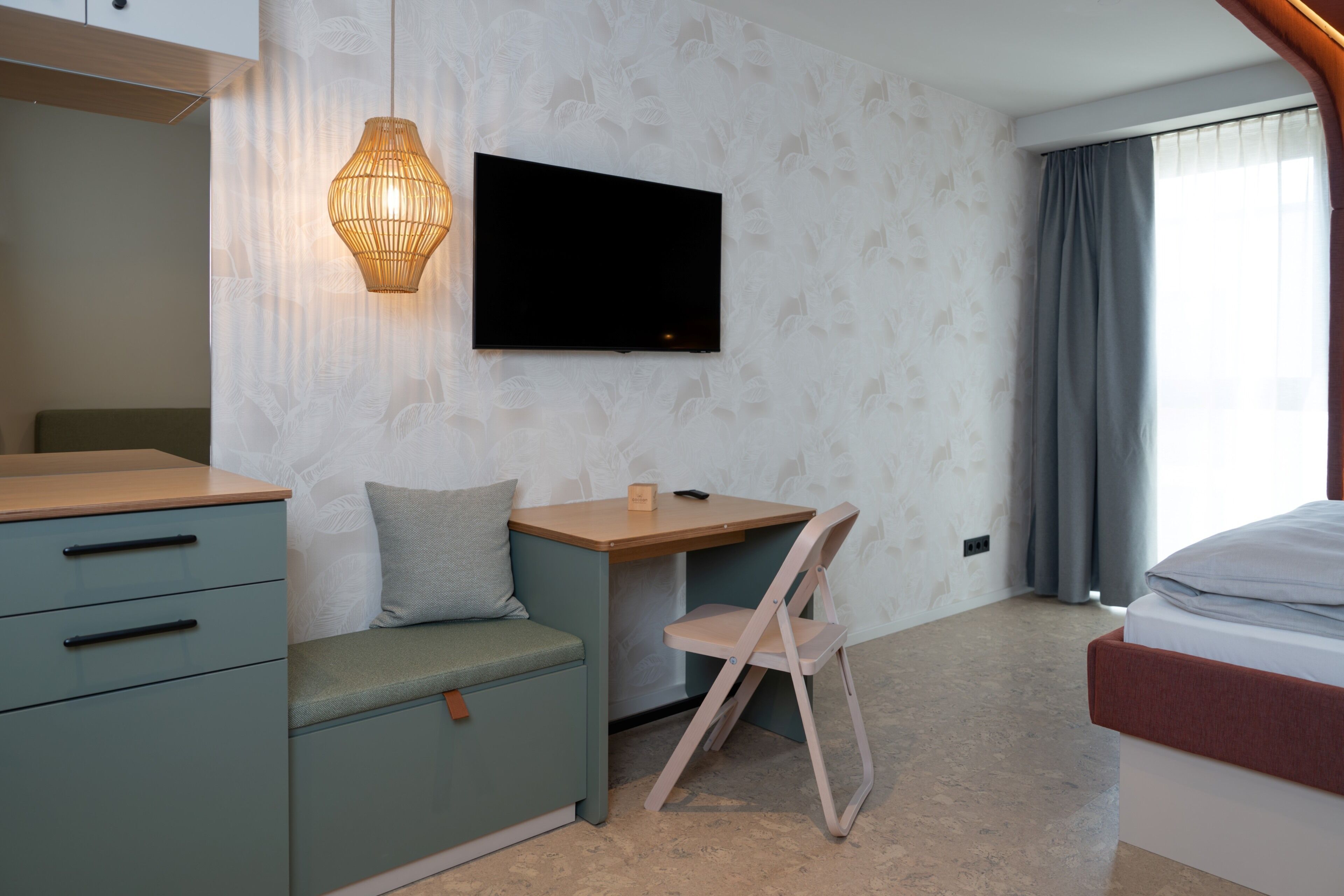 Una habitación de hotel moderna con una cama, un escritorio, una silla, un televisor y un armario.