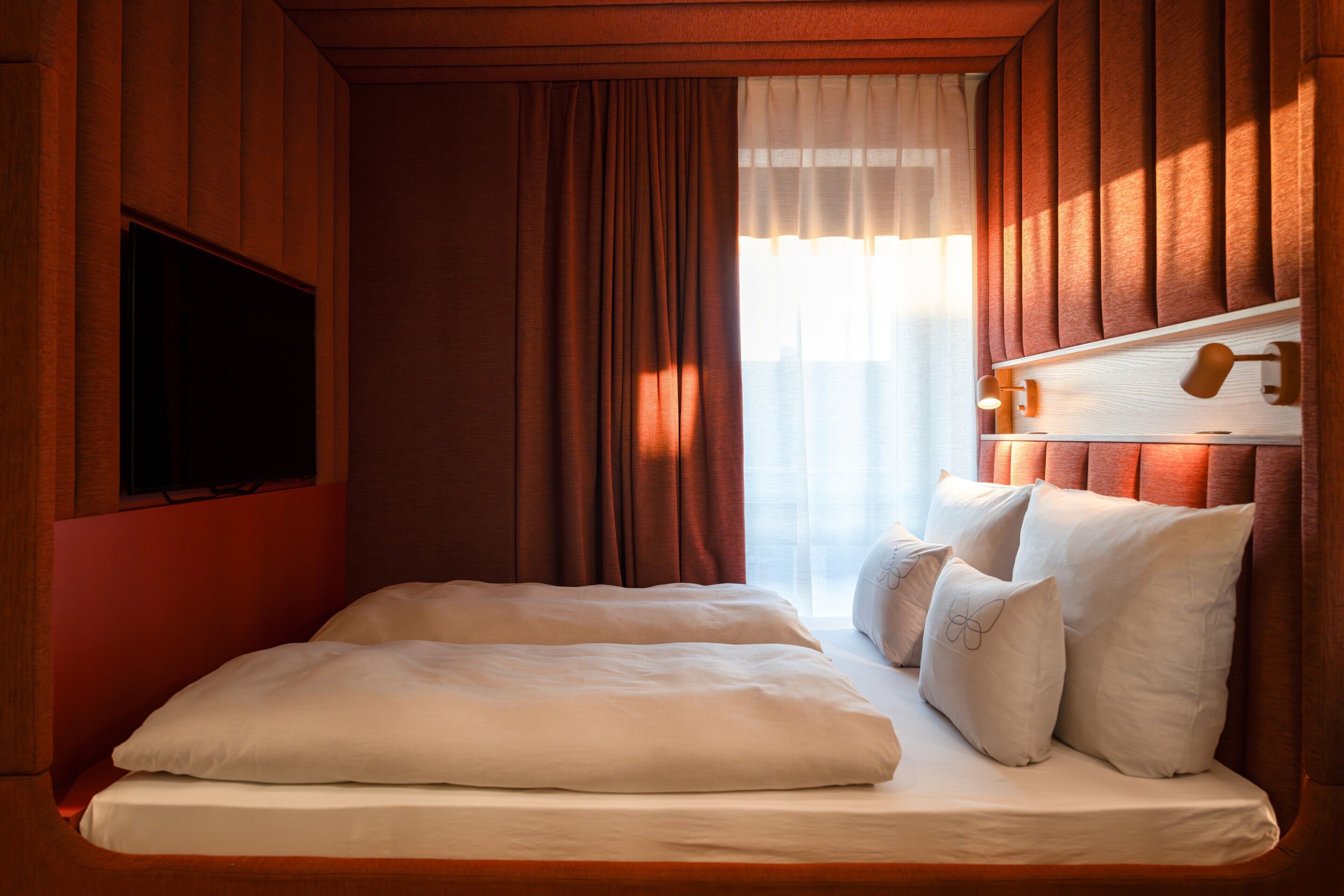 Une chambre avec un lit, des rideaux, une télévision et une tête de lit dotée de lampes.