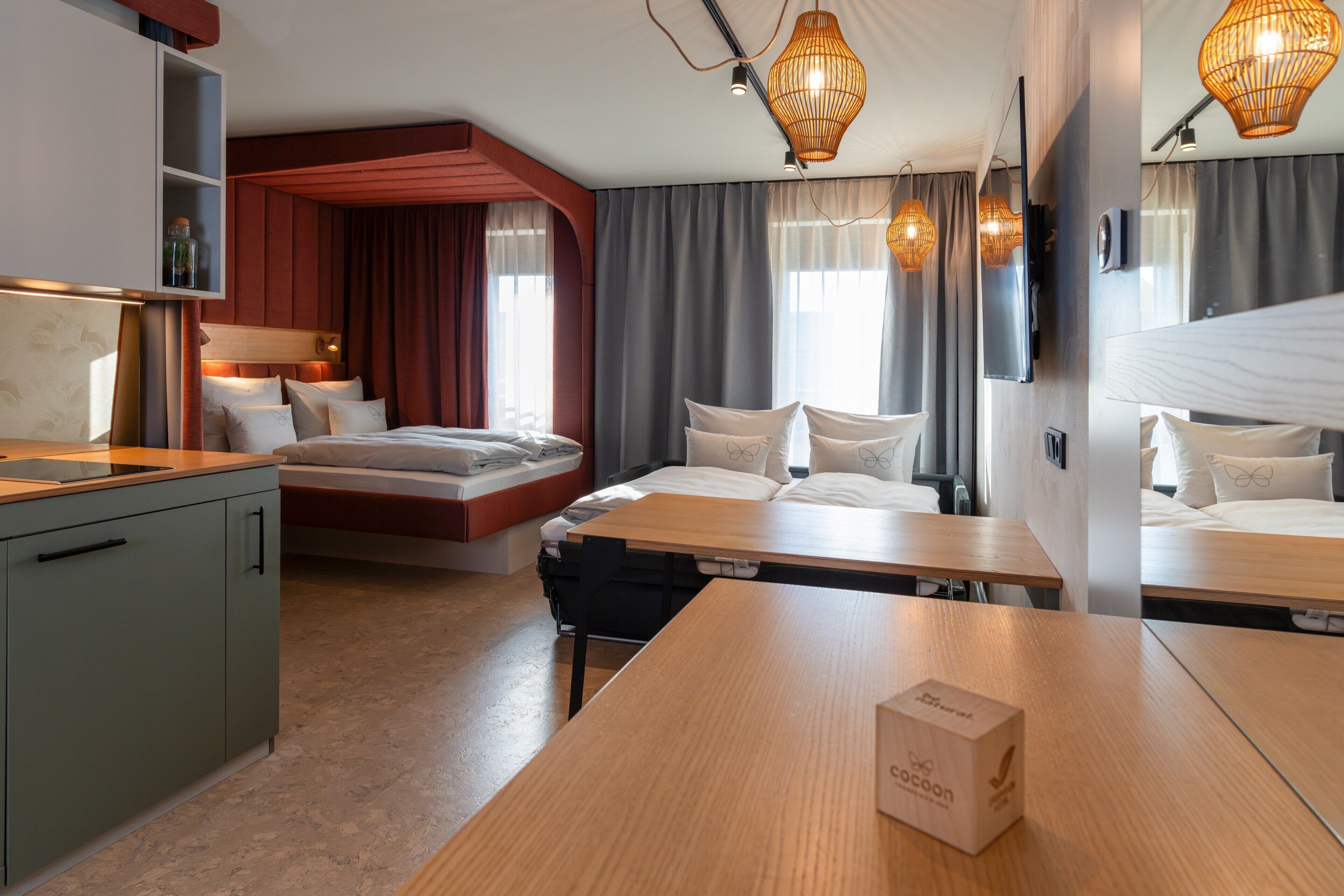 Ein Hotelzimmer mit Bett, Nachttischen, Schreibtisch, Fernseher und einem Regal mit Gegenständen.