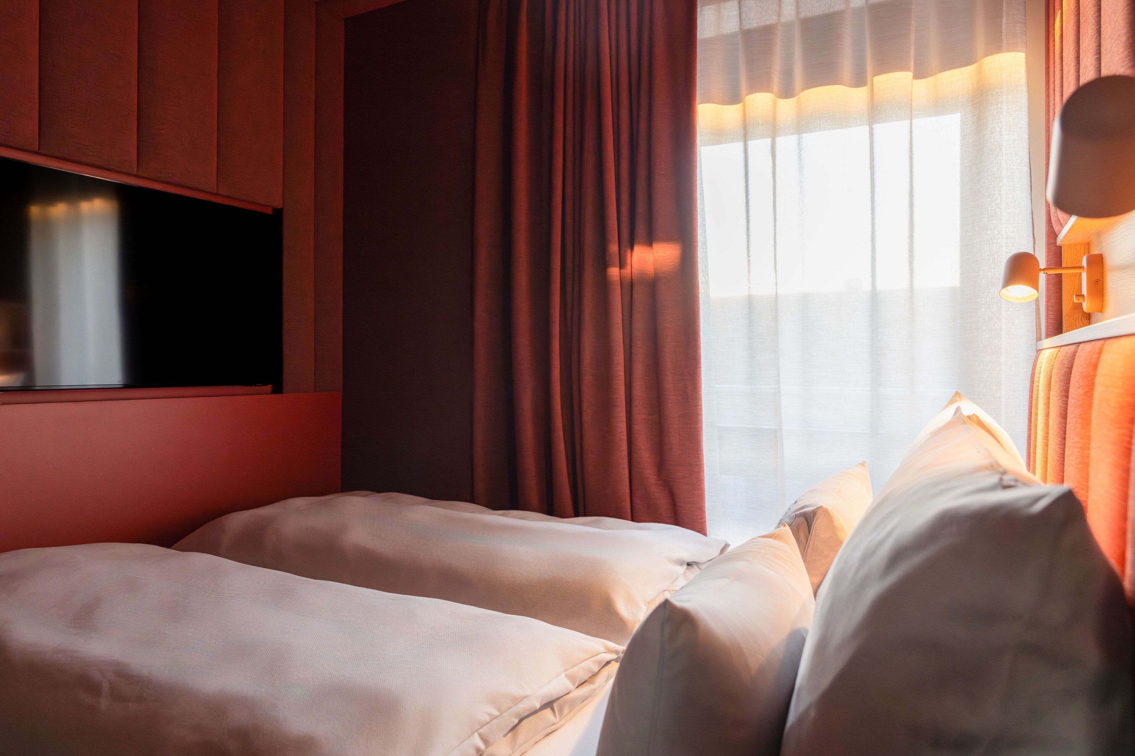 Habitación de hotel con cama, cortinas, ventana y lámpara de pared.