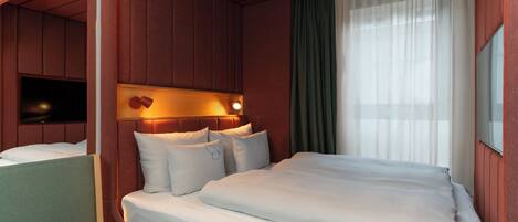 A hotel room with a bed, a seating area, a television, and a window with curtains.