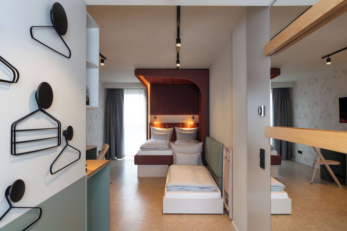 A compact hotel room with a bed, bedside tables, a desk, and a mirror.