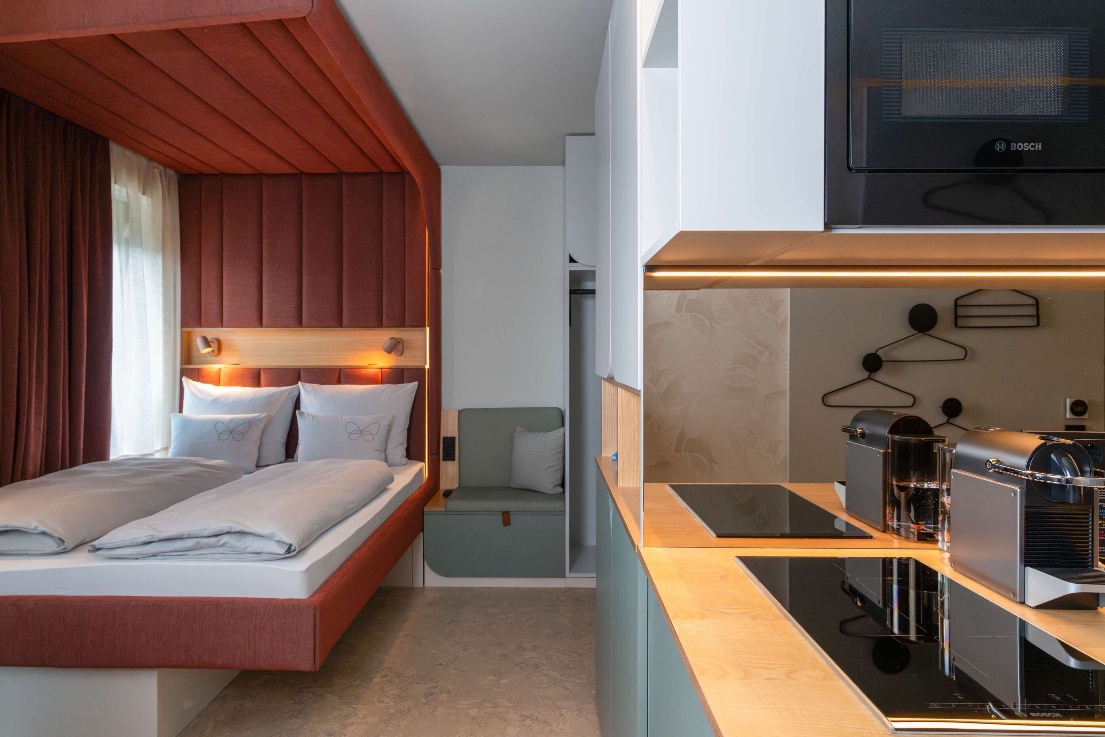 Habitación de hotel compacta con cama, zona de estar, kitchenette y televisor.