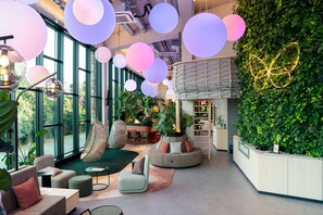A modern interior with large windows, a reception desk, and a green wall with plants. - Cocoon München Theresienwiese (Munich)