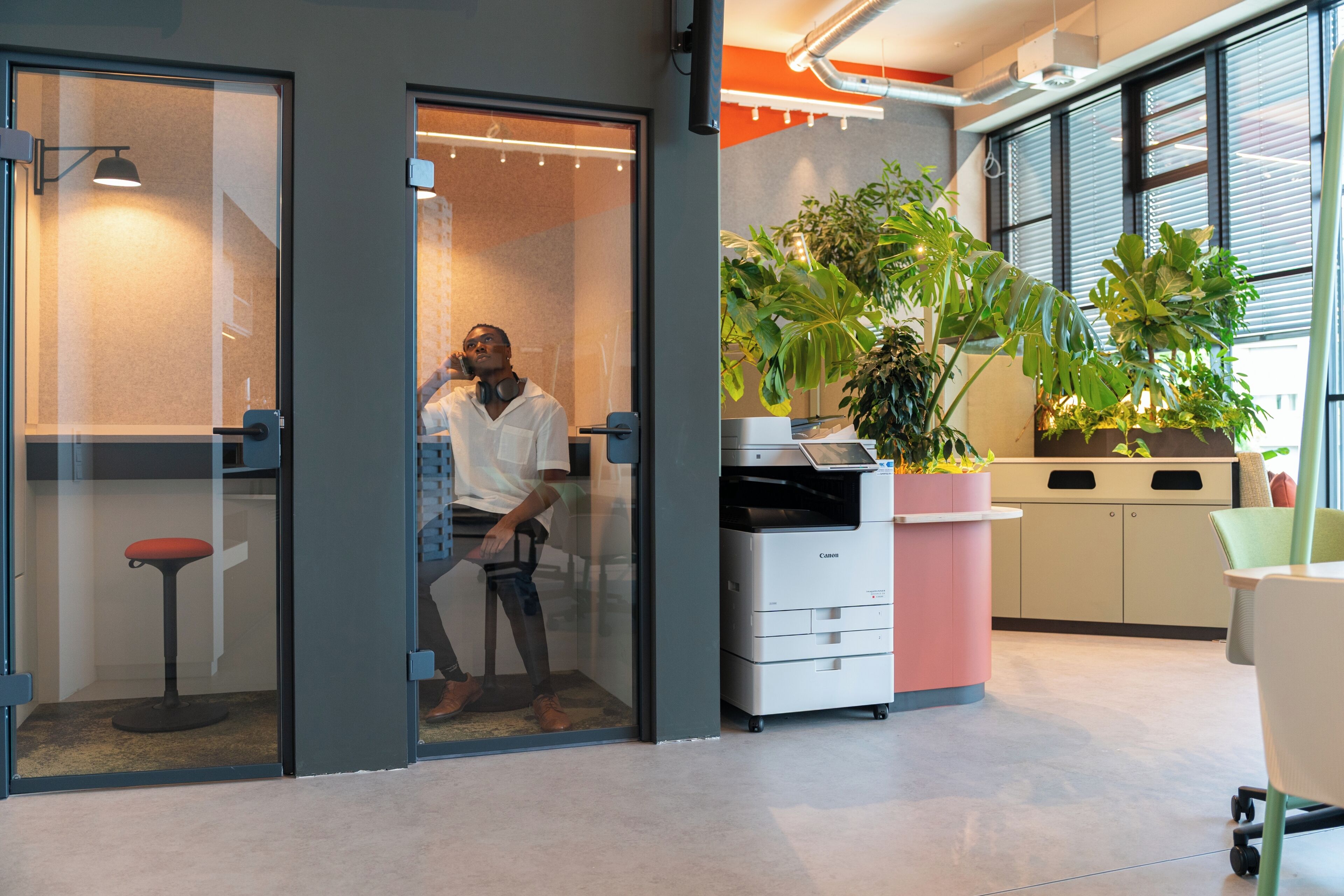 Un espacio de oficina moderno con un separador de vidrio, una impresora y plantas en macetas.