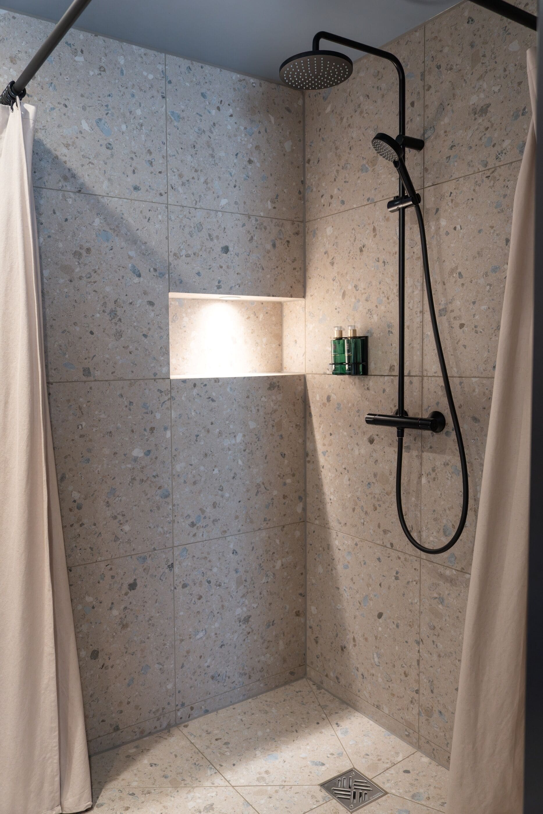Une douche équipée d’un pommeau de douche à main, d’un robinet mural et d’une étagère pour les articles de toilette.