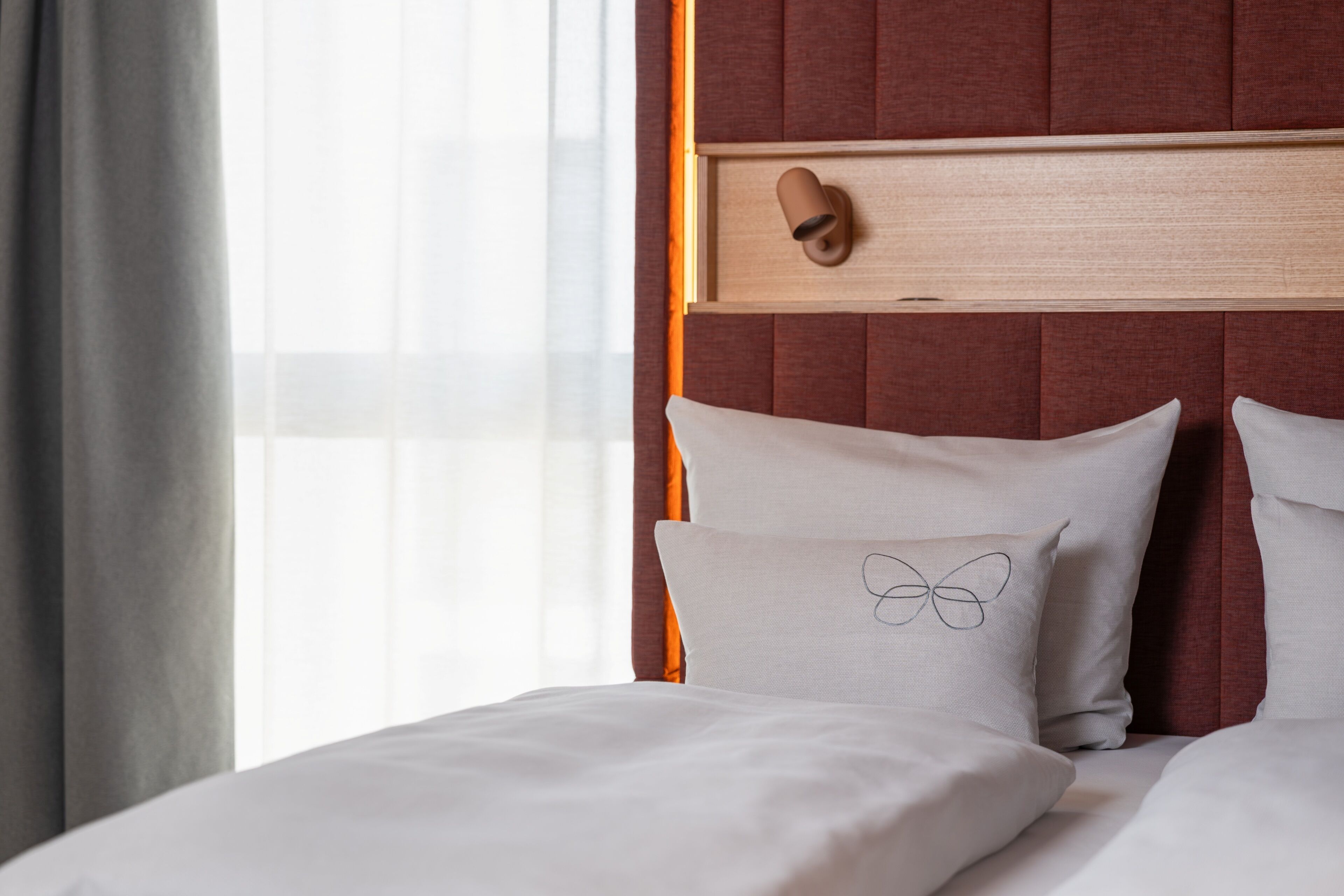 A hotel room with a bed, a headboard, and a window with curtains.