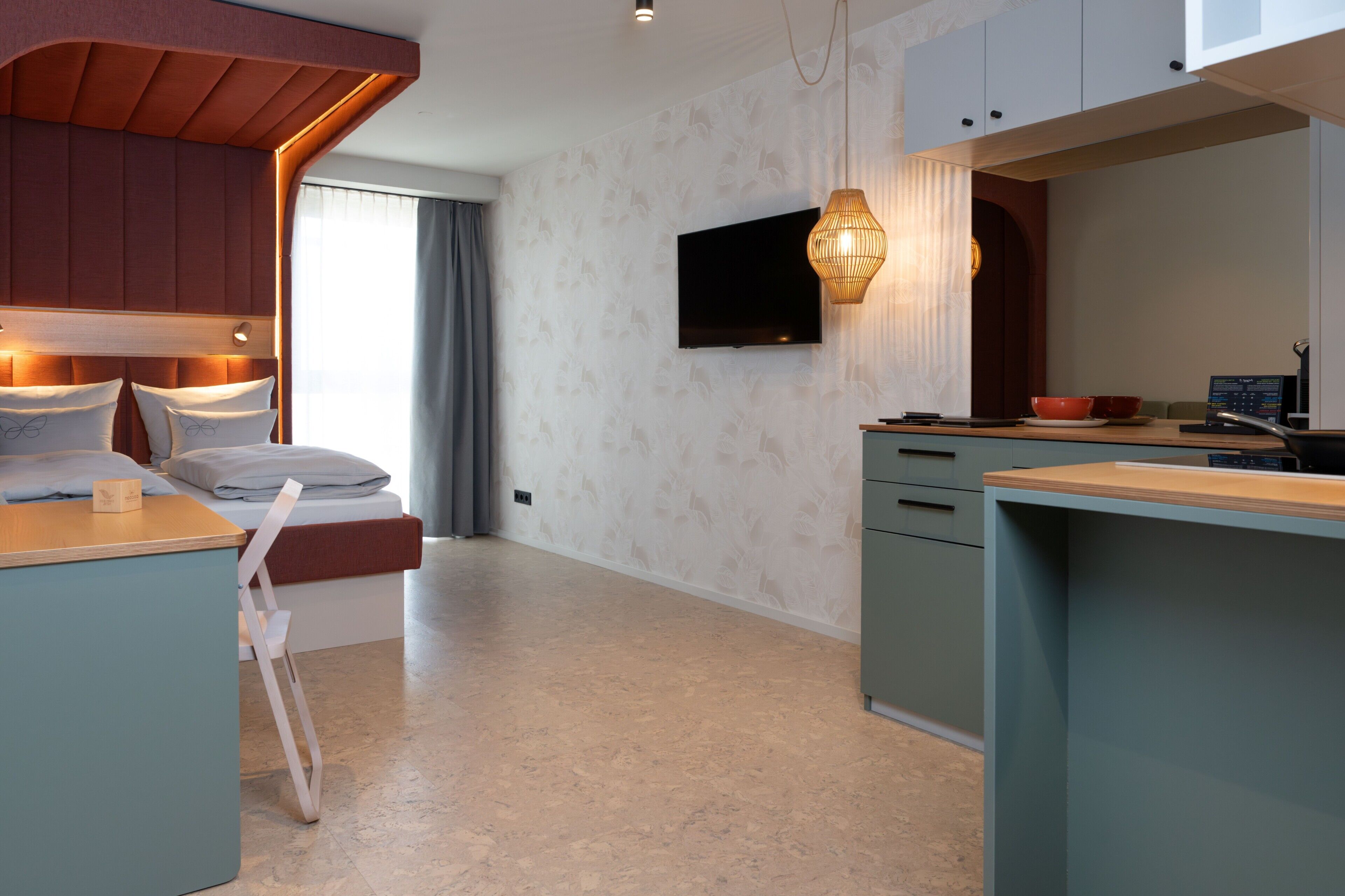 Habitación de hotel moderna con cama, escritorio, televisor y zona de cocina.