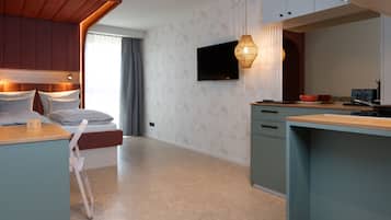 Habitación de hotel moderna con cama, escritorio, televisor y zona de cocina.