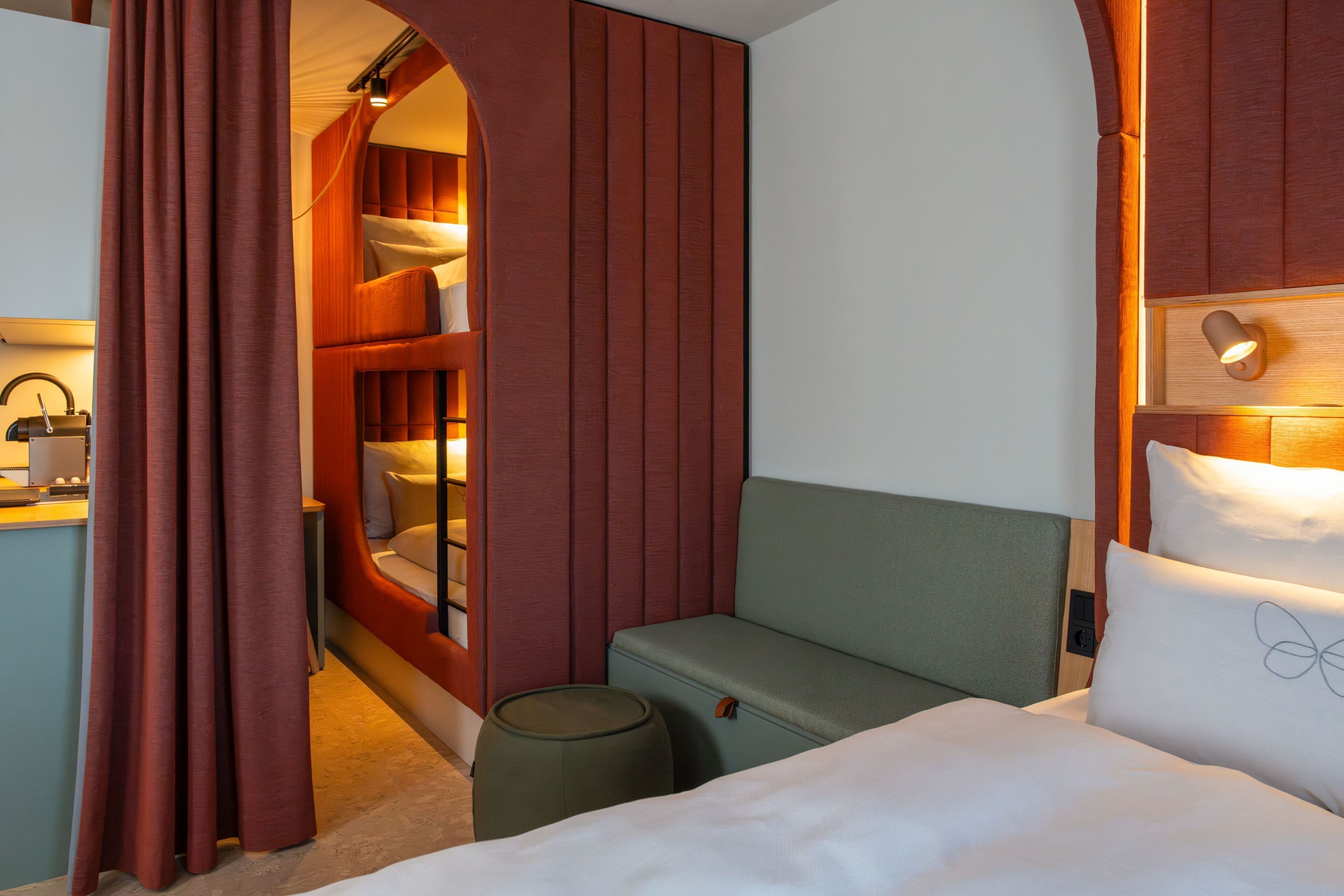 A hotel room with a bed, a small seating area, a vanity with a mirror, and a wardrobe.