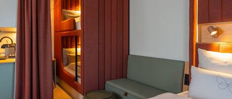 A hotel room with a bed, a small seating area, a vanity with a mirror, and a wardrobe.