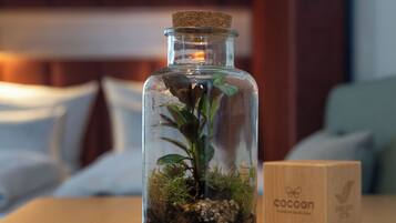 Una botella de vidrio con una planta, una caja de madera y un fondo desenfocado de una habitación con cama y almohadas.