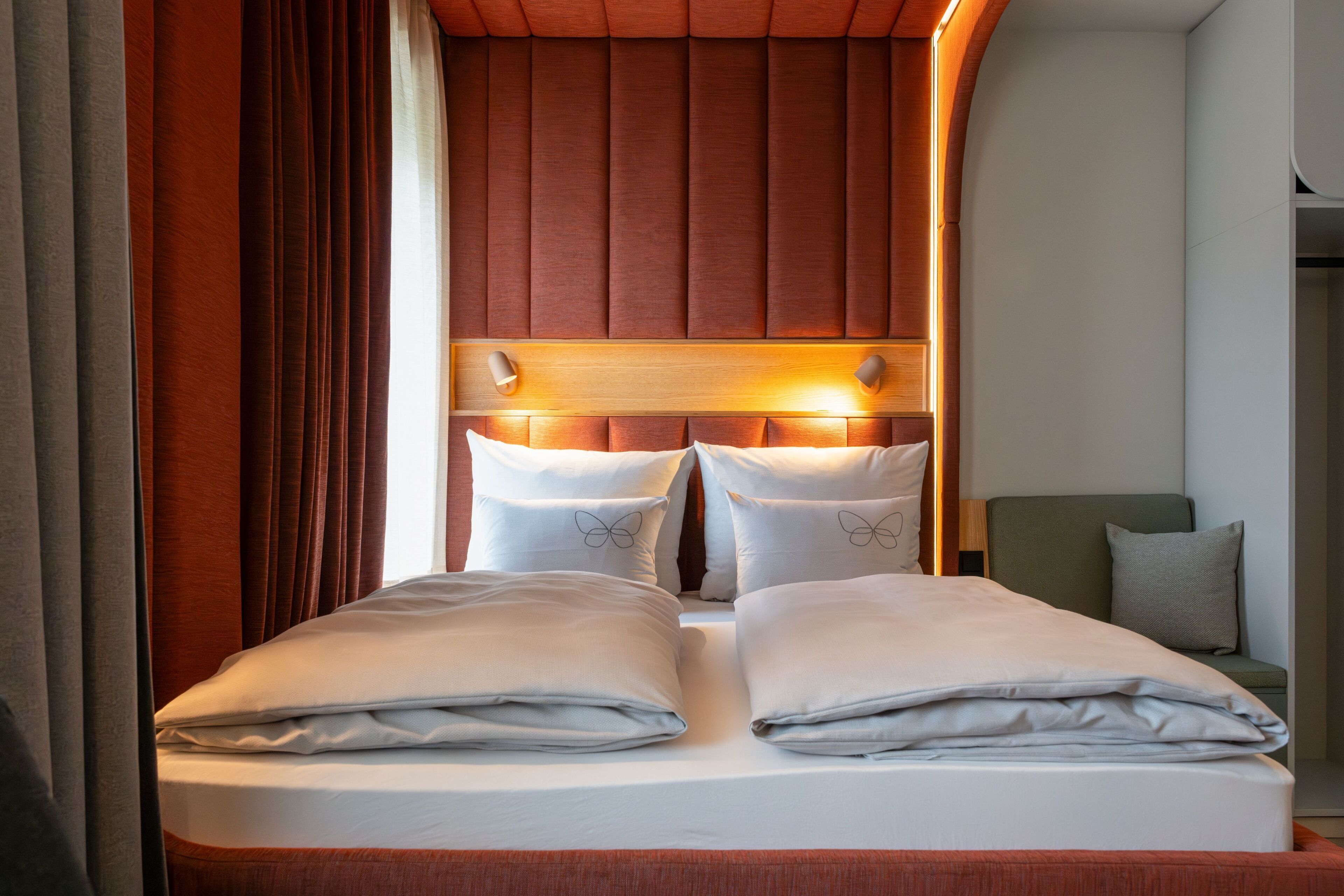 A neatly made bed with pillows, a headboard with built-in lighting, and a green chair in a hotel room.