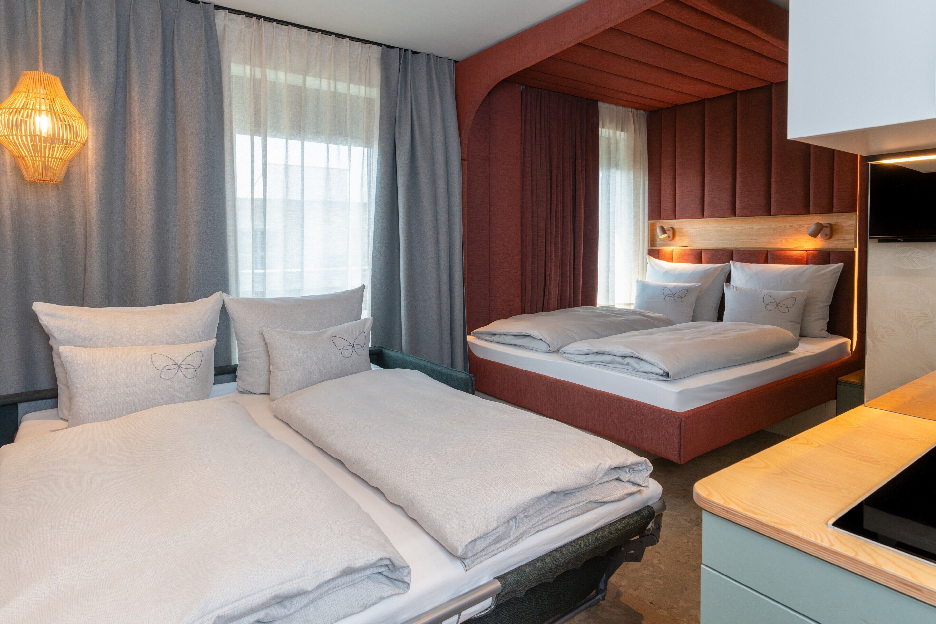 Ein Hotelzimmer mit zwei Betten, einem Holz-Kopfteil, einem Flachbildfernseher und einem großen Fenster mit Vorhängen.