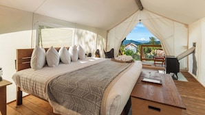 Een tentaccommodatie met een bed, kussens, een tafel en uitzicht op een berg.