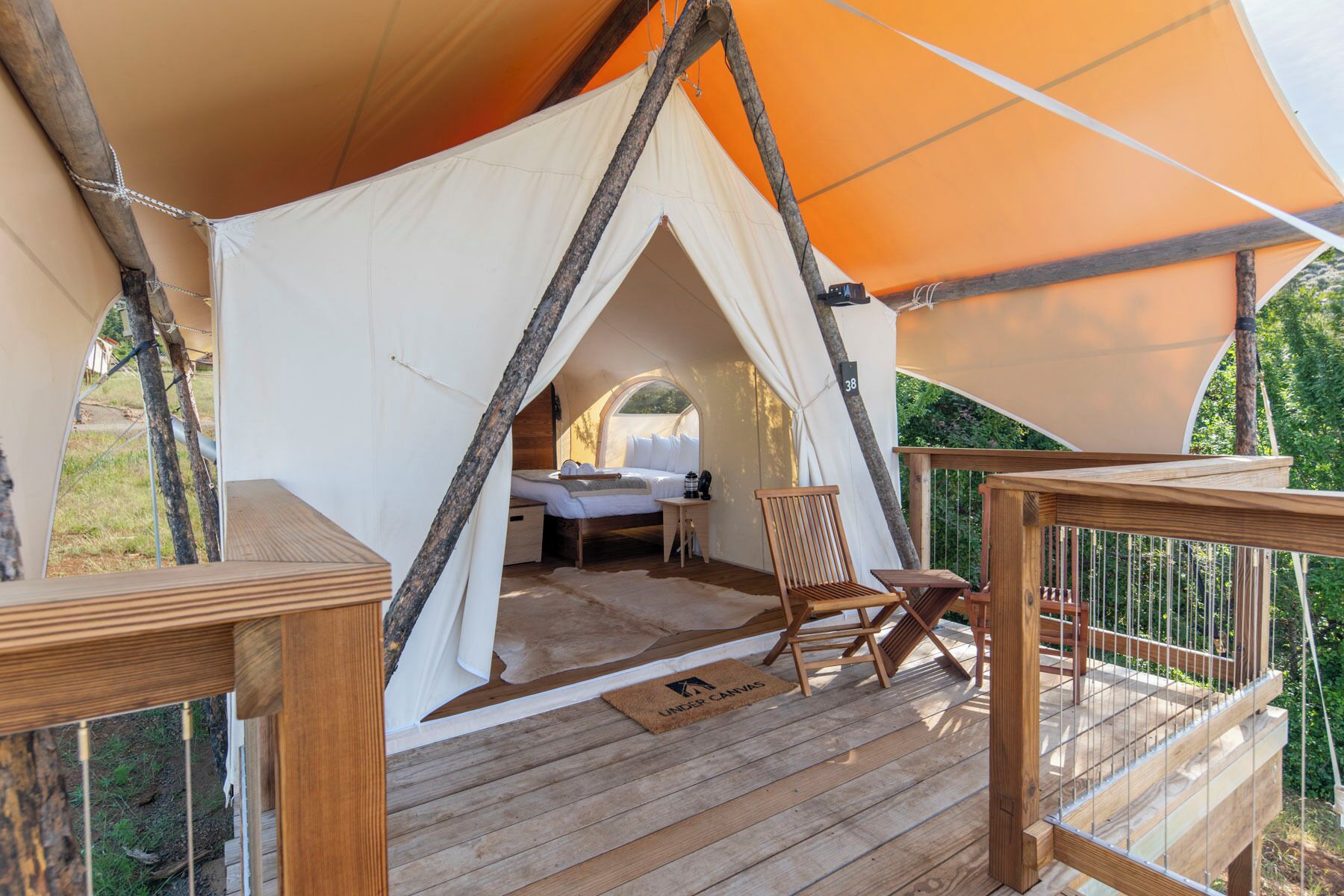 A tent with a bed, a small table, and a chair on a wooden deck.