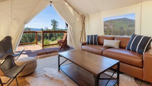 A cozy room with a leather sofa, a wooden coffee table, and a view of a forest and mountains through a large window.