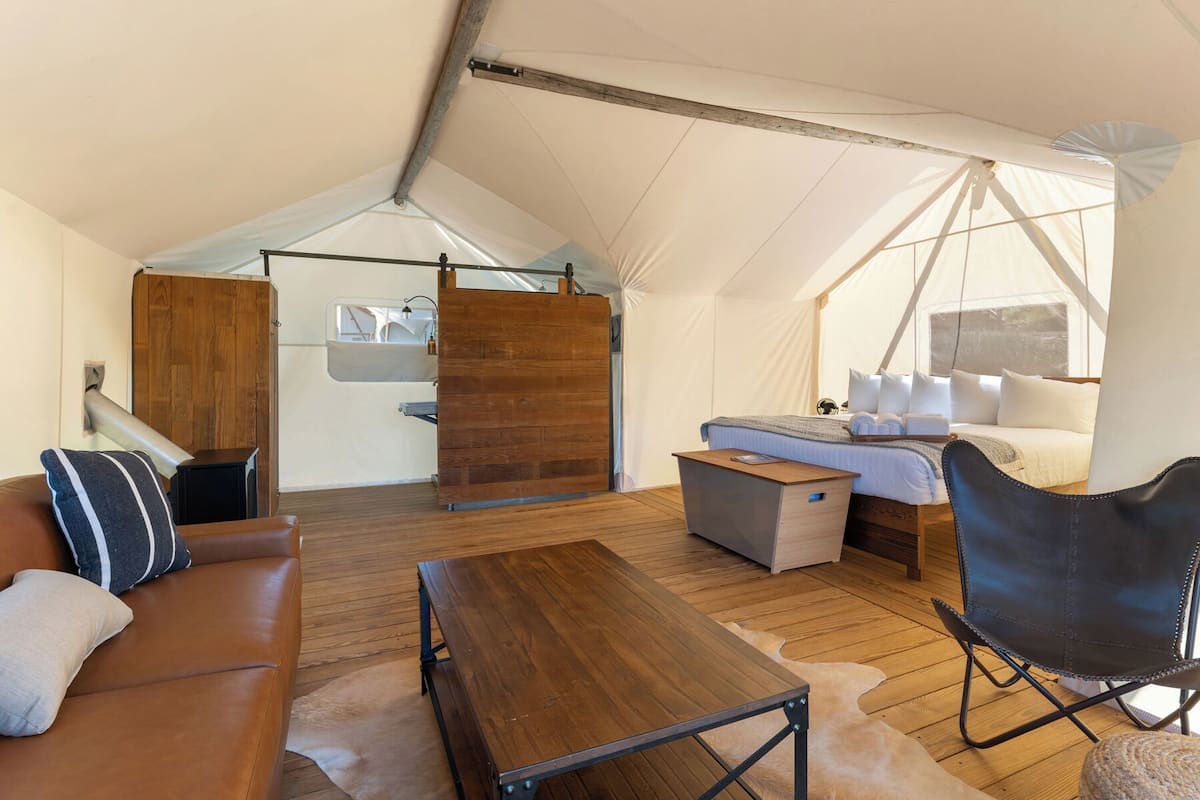 Un hébergement sous tente doté d’un plancher en bois, d’un canapé, d’une table, d’un lit avec des oreillers et d’une chaise.