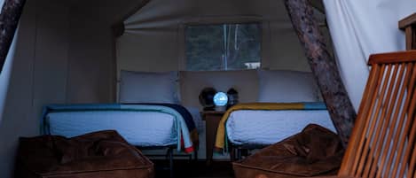 Une tente équipée de deux lits, d’une fenêtre, d’un ventilateur et d’une chaise.