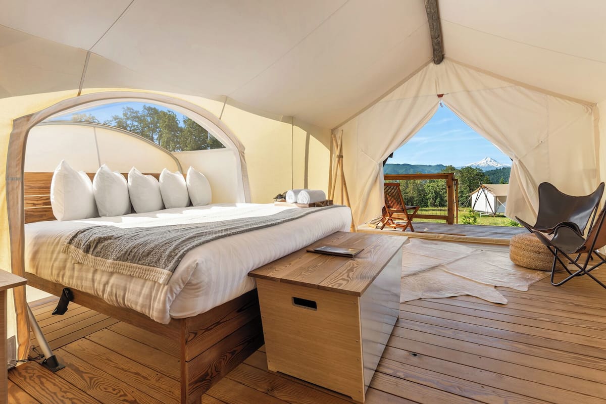 Un hébergement sous tente comprenant un lit, une terrasse en bois et une vue sur une montagne.