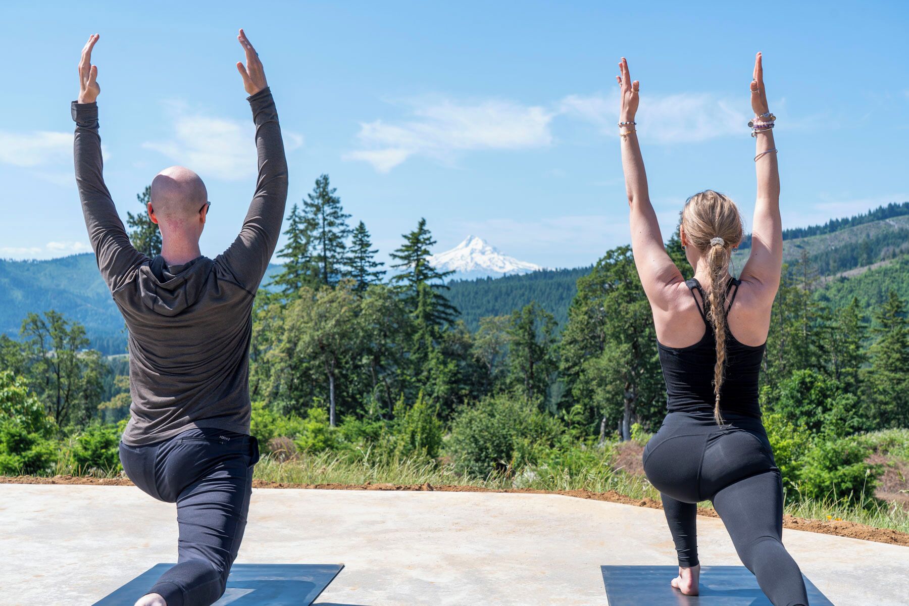 Two people performing yoga on mats with a mountain and forest in the background.