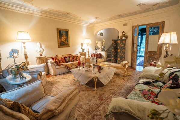 Une pièce à l’ambiance traditionnelle, avec un ensemble de canapés, une table ronde décorée de bougies et un escalier menant à une autre pièce.
