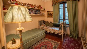Quarto aconchegante com uma cama de solteiro, um pequeno sofá, uma luminária e prateleiras com brinquedos de pelúcia.