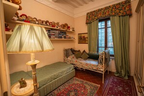 Een gezellige slaapkamer met een eenpersoonsbed, een kleine zithoek, een lamp en planken met knuffelspullen.