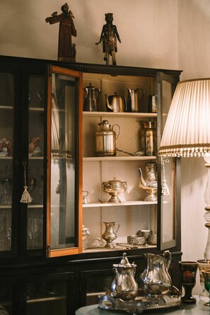 Une pièce dans laquelle se trouve un buffet en bois où sont exposés différents services à thé en argent et des articles en verre.