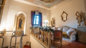 Uma sala imponente com escadaria, decorações elaboradas, um sofá e uma estátua.