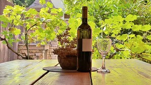 Una botella de vino y una copa sobre una mesa de madera, con una chimenea de piedra al fondo.