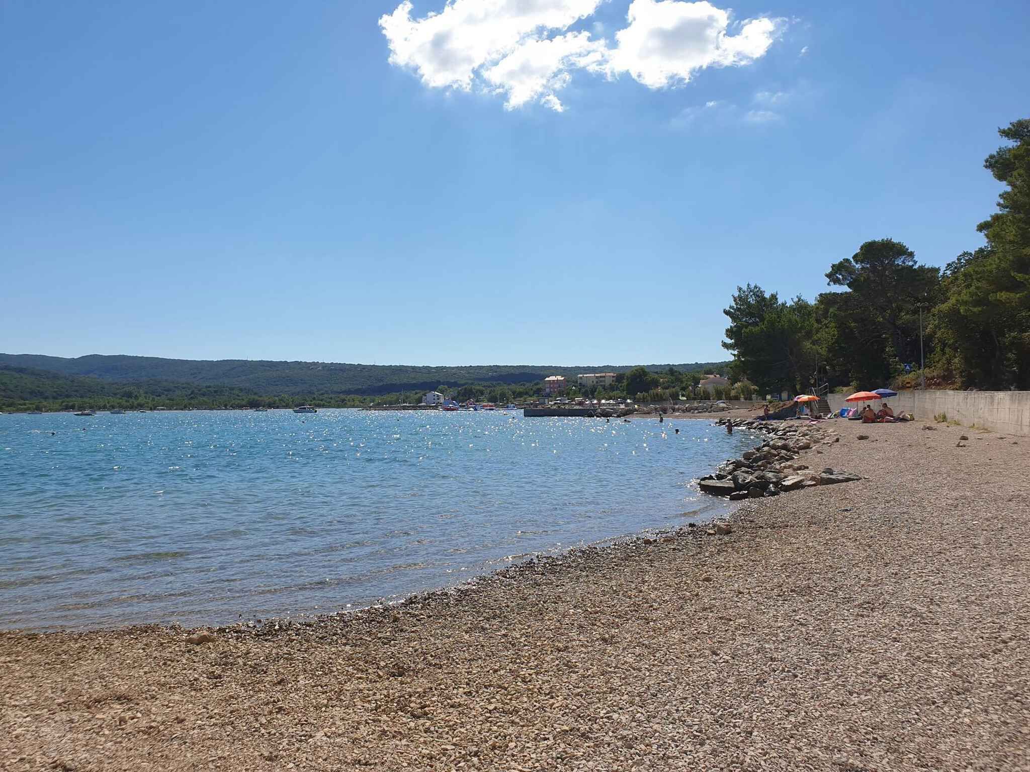 Ein Kiesstrand mit blauem Himmel und ruhigem Wasser.