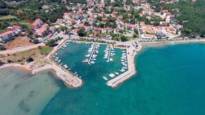 Vista aérea de un pueblo costero con un puerto deportivo, edificios residenciales y una zona de playa.